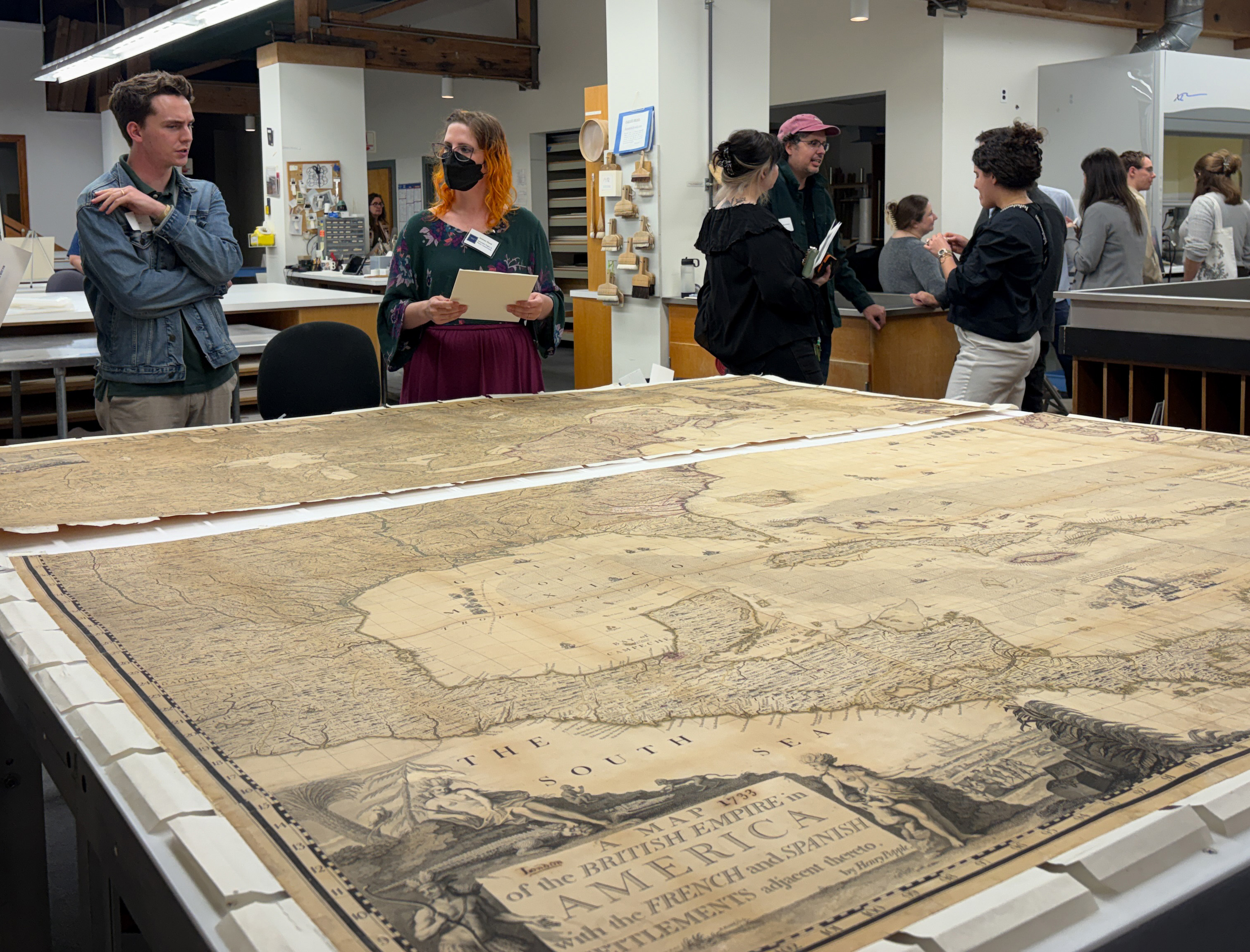 Historic map spread across a large table at a CCAHA open house, with visitors gathered around it.