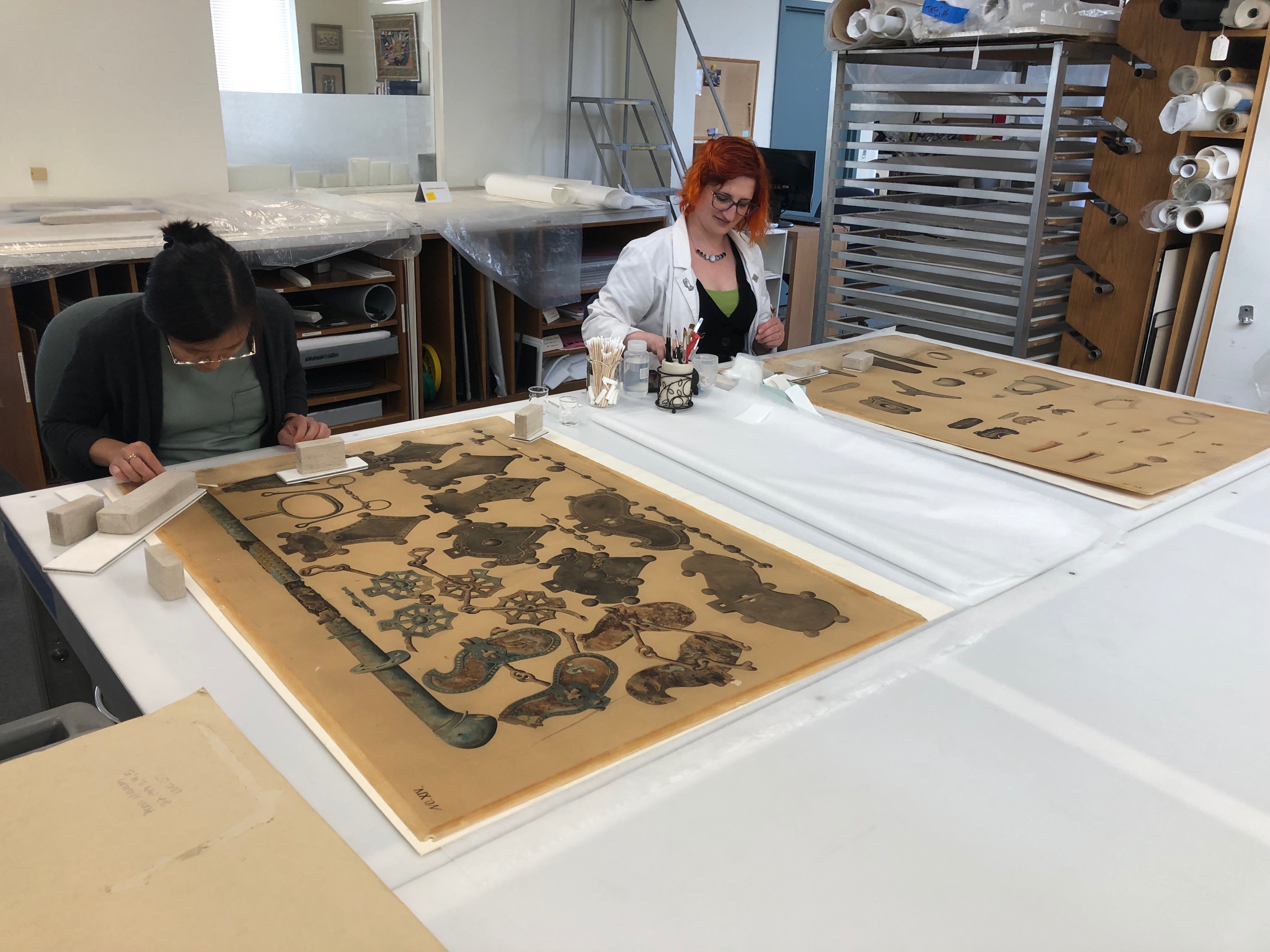 CCAHA Conservation Technician Binh-An Nguyen and Associate Conservator Joanna Hurd work together on an 1893 Japanese watercolor from the Penn Museum's collections