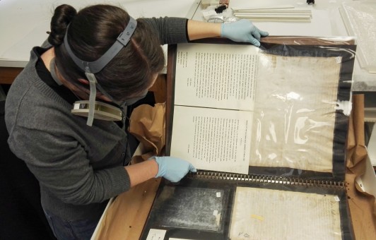 Masked conservator examines laminated volume