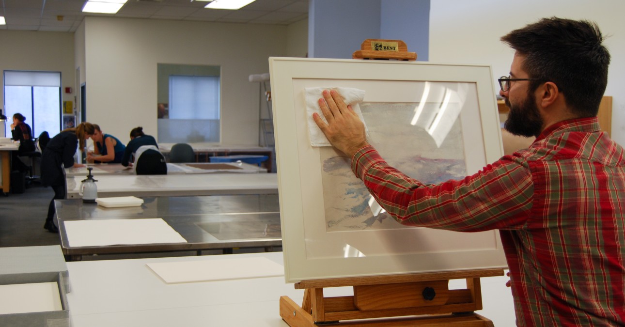 Man cleans glazing of framed watercolor
