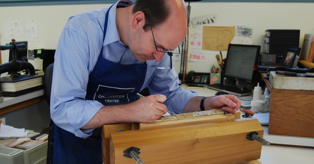 Conservator wearing magnifiers works on spine of book