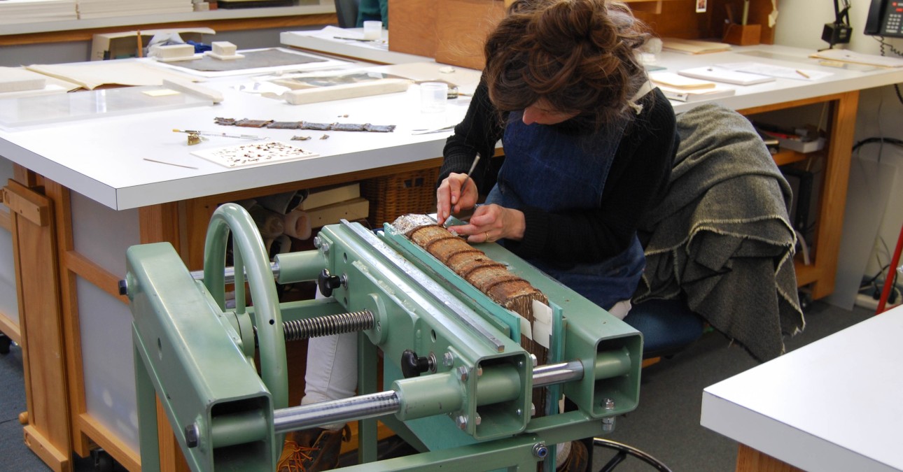 Conservator at a book press works on spine of manuscript