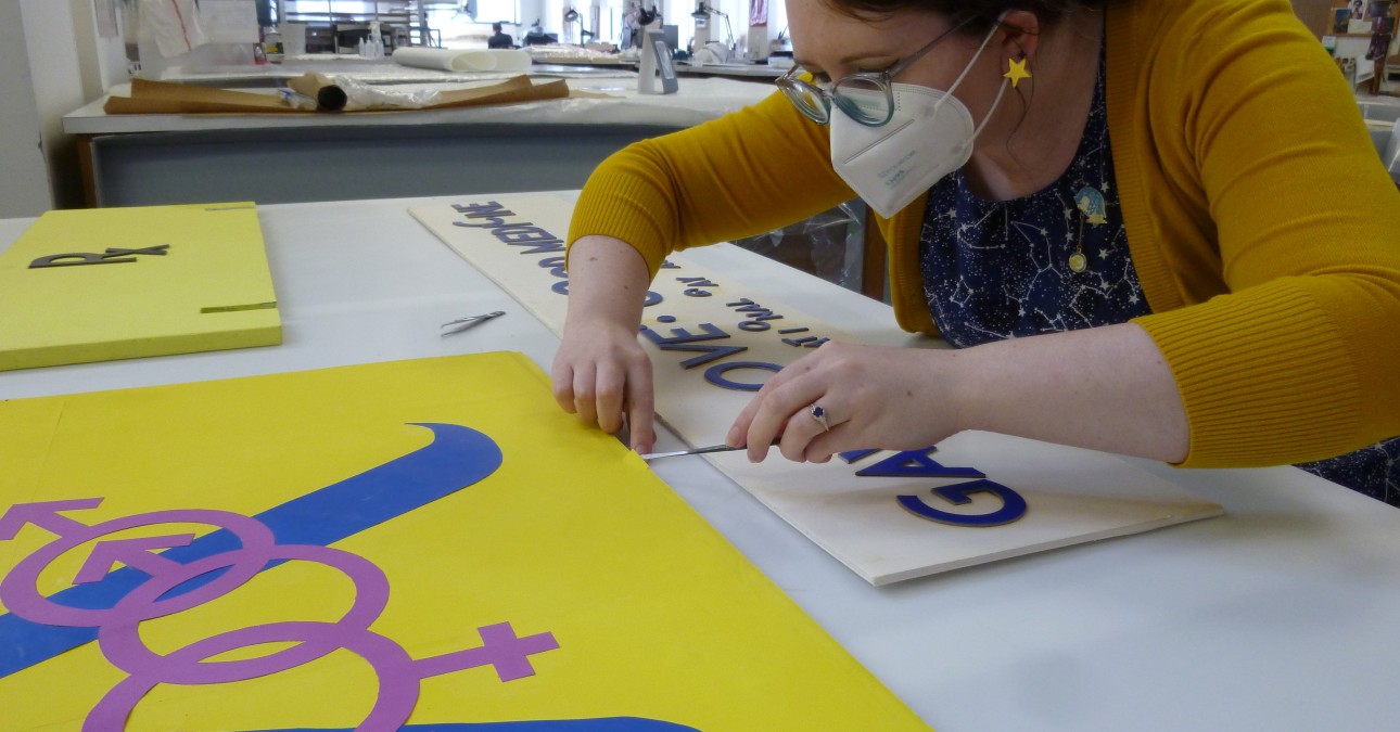 Picture of Paper Conservator Chloe Houseman working on a bright yellow, blue, and purple sign