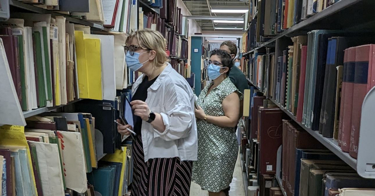 Three people examining shelves in a library.