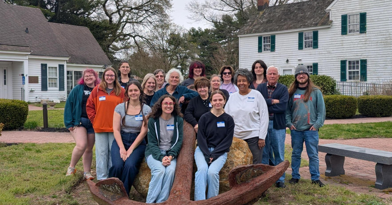 group of workshop attendees posing together outdoors behind a large, rusted anchor at the Cape May County Historical & Genealogical Society.