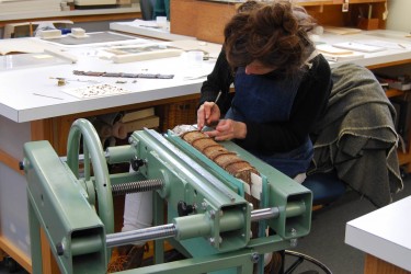 Conservator at a book press works on spine of manuscript