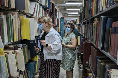 Three people examining shelves in a library.