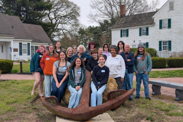 group of workshop attendees posing together outdoors behind a large, rusted anchor at the Cape May County Historical & Genealogical Society.